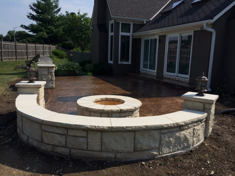 Curved stone seating wall with a built-in fire pit beside a stamped patio